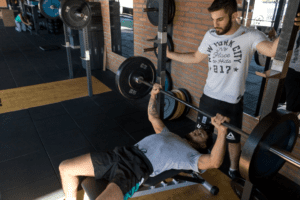 A man lifting a barbell with his fitness trainer